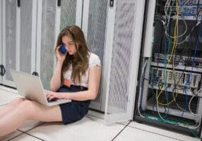 Woman checking the servers with laptop and talking on phone in data center